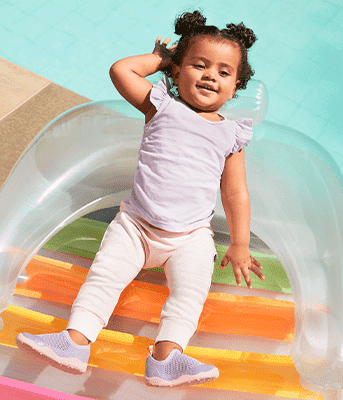Bebê de cabelo preso deitada em uma bóia na beira da piscina